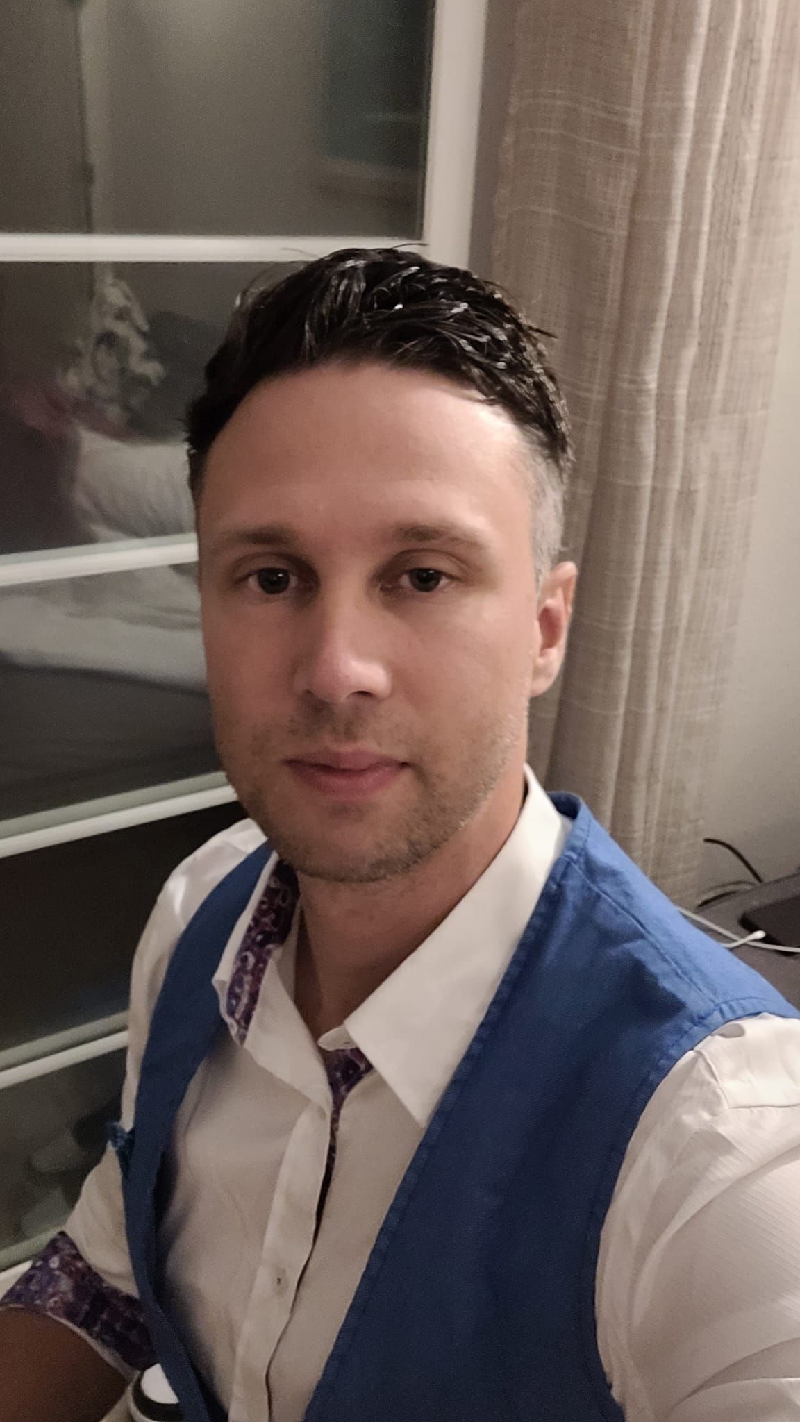 Een man in een wit overhemd en een blauw vest maakt een selfie.