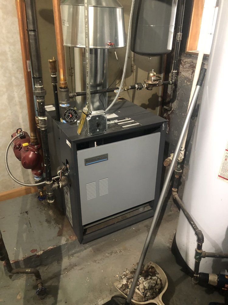 A boiler in a basement with connected pipes, a chimney, and a hot water tank. Gray and brown tones.