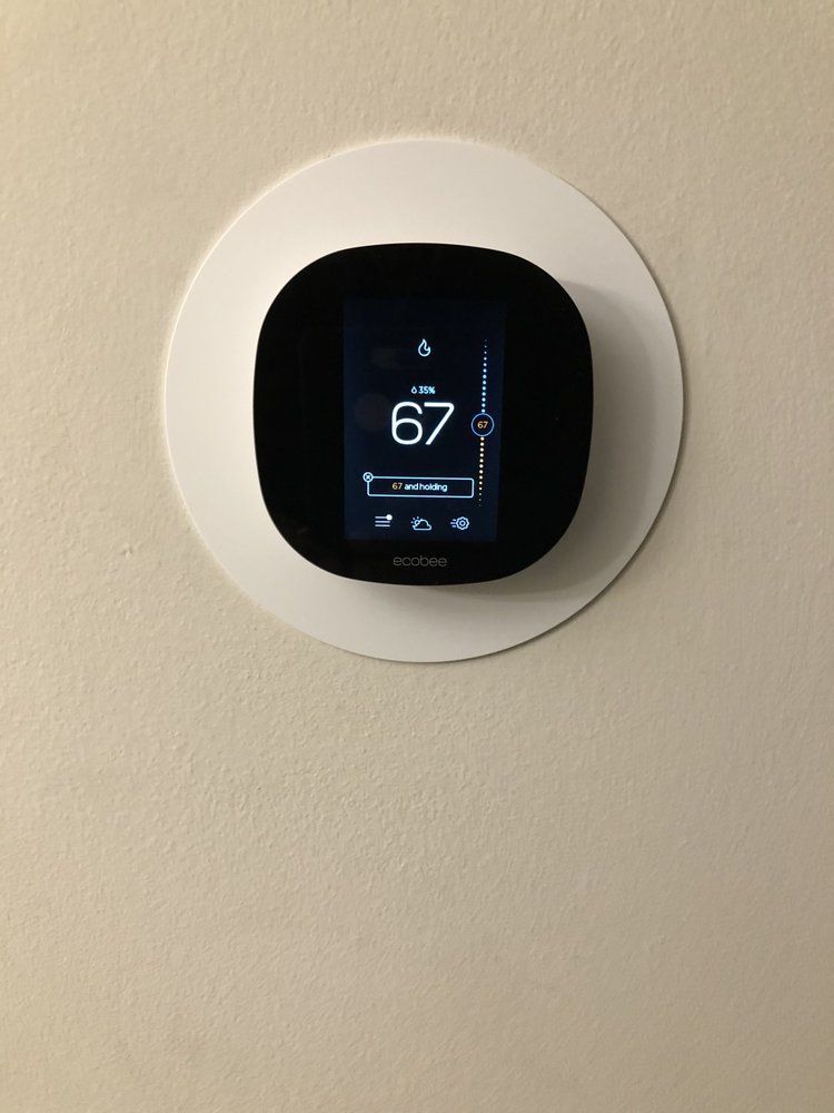 Smart thermostat on a beige wall, displaying temperature 67 degrees Fahrenheit.
