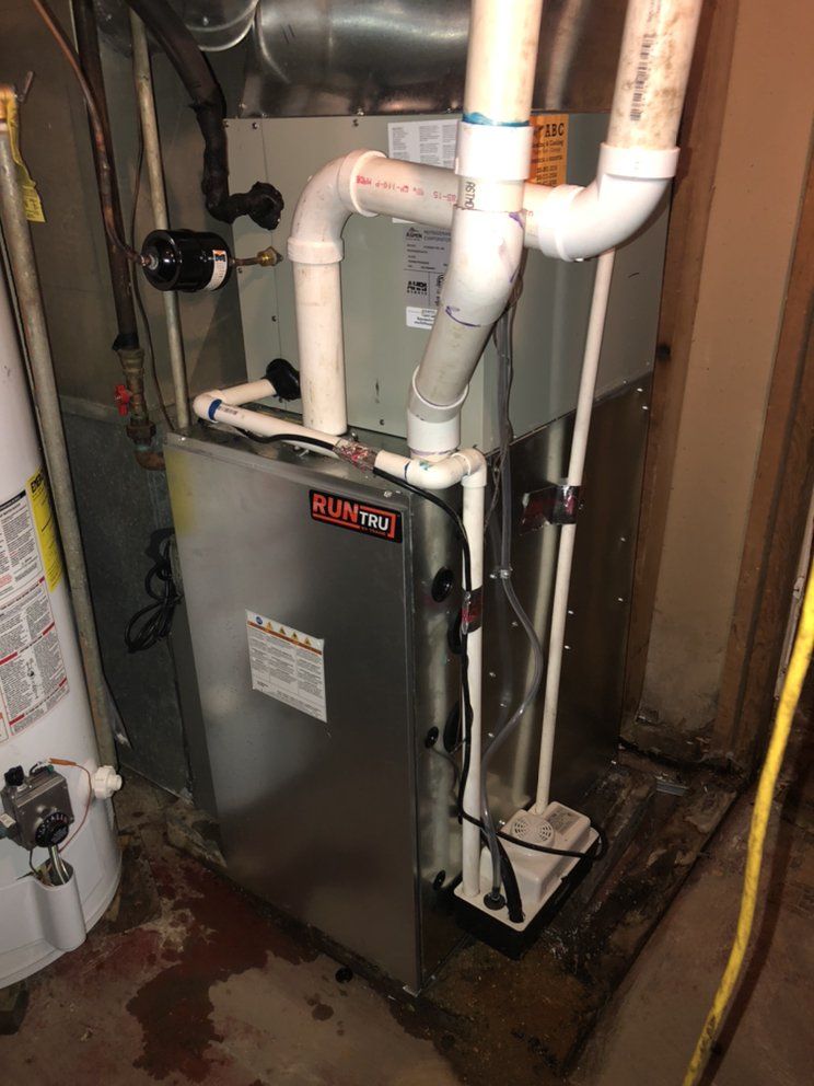 Furnace in a basement next to a water heater. White pipes, silver metal, and various wires are visible.