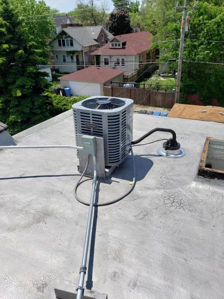 Air conditioning unit on a flat rooftop; residential neighborhood in the background.