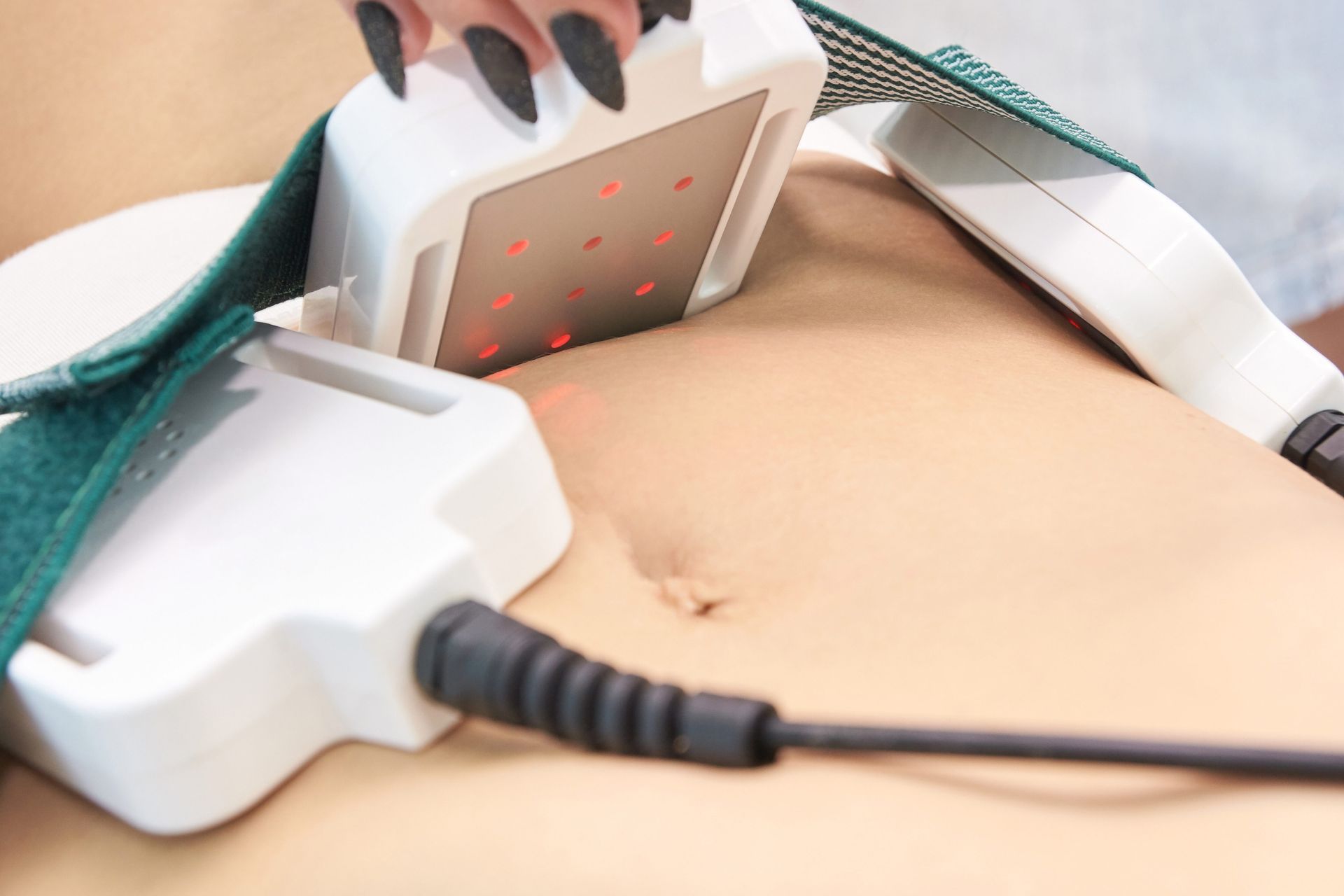 White devices strapped to a person's abdomen. One device shows red lights. Black cable attached.