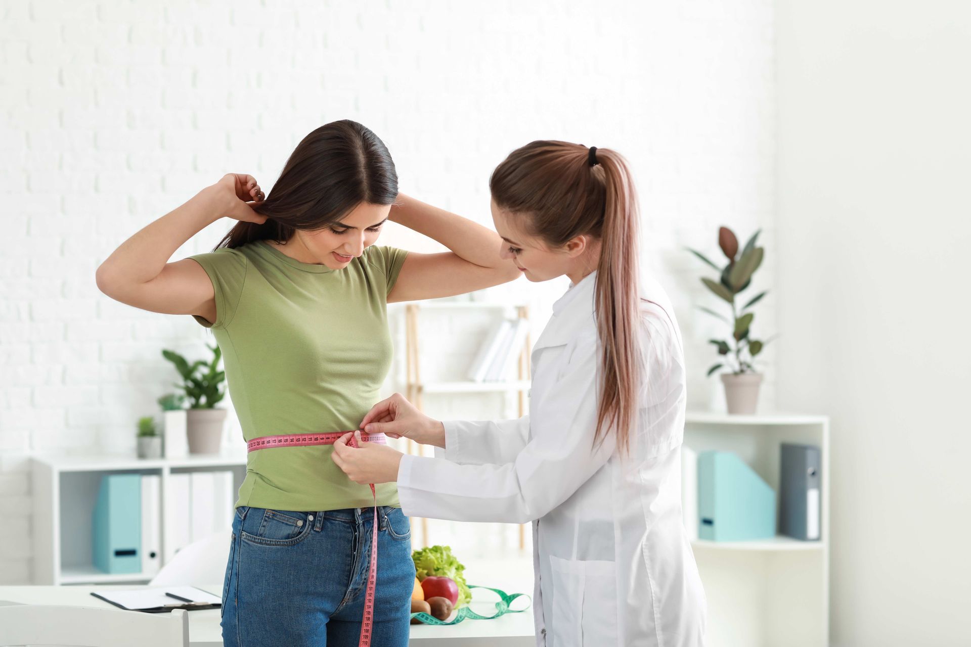 Woman in green shirt being measured by a person in a white coat, indoors.