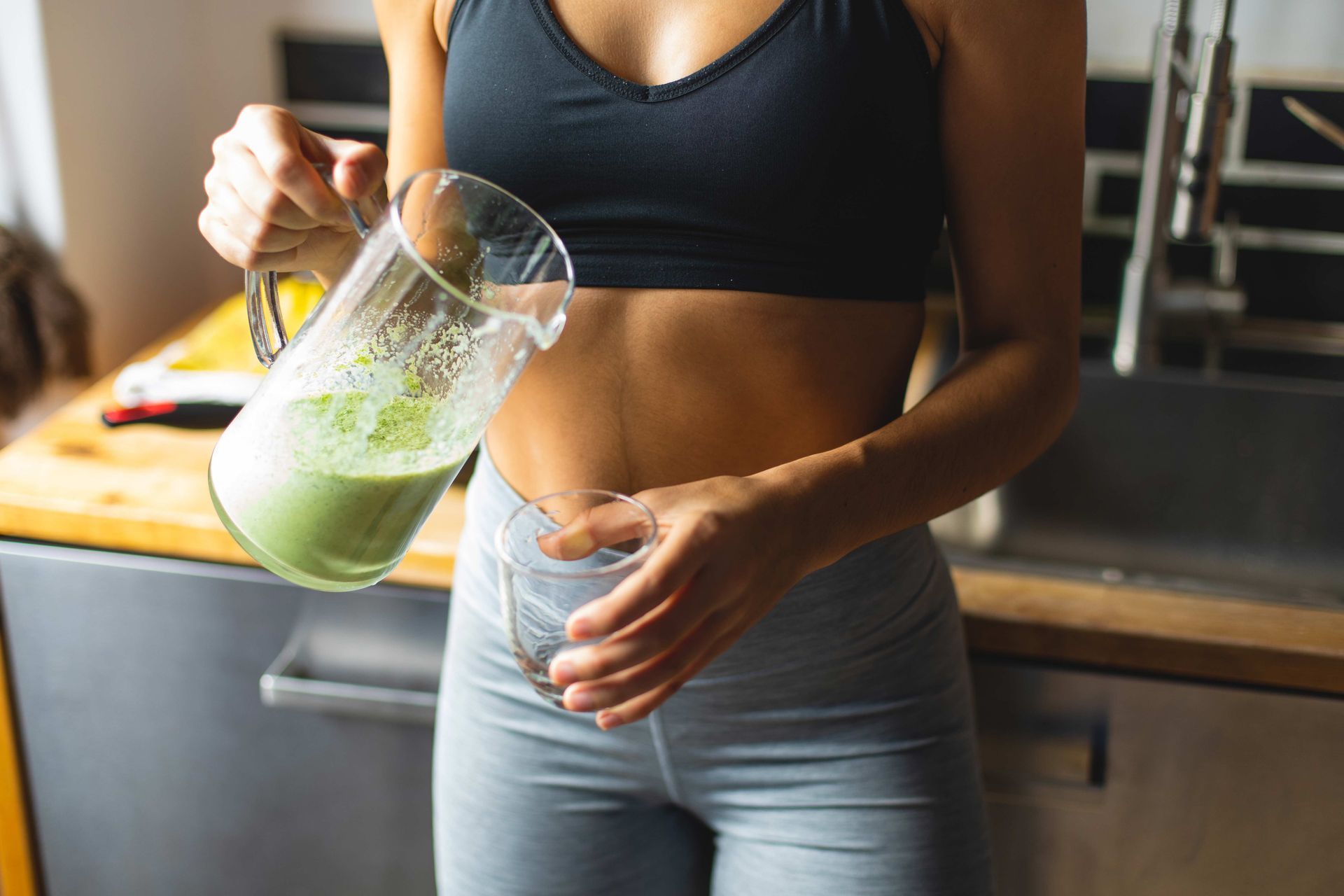 Woman pouring green smoothie into a glass in kitchen.