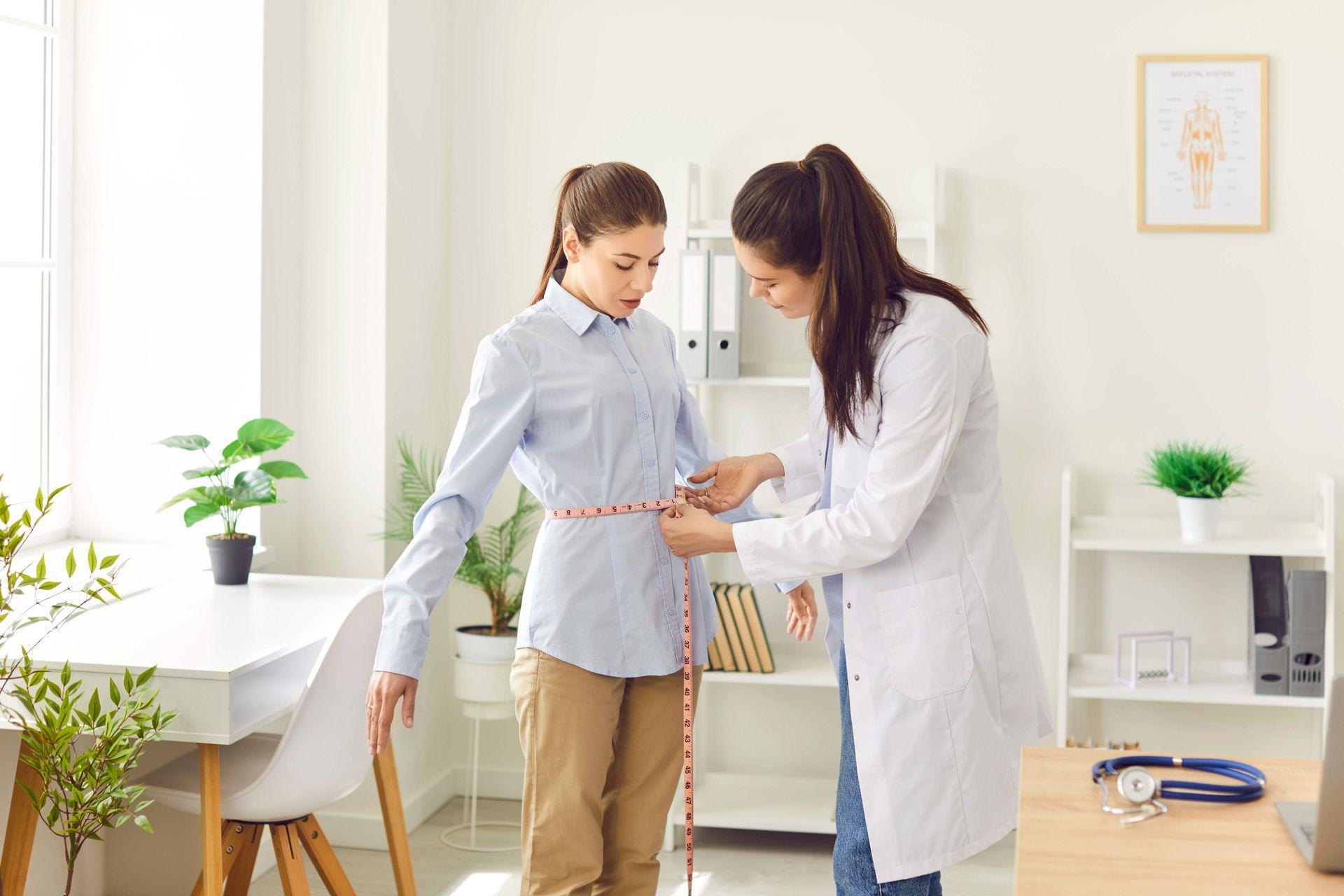 Doctor measuring a patient's waist with a tape measure in a medical office.