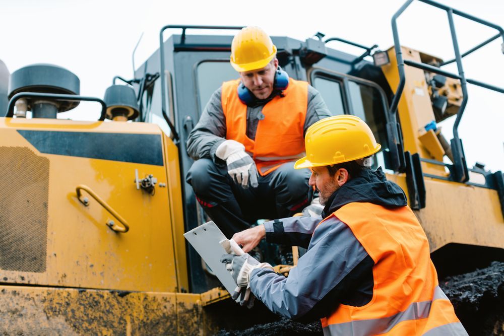 Two Construction Workers Are Sitting On A Bulldozer And Looking At A Clipboard — All Hours Vac Truck In Mt Morgan, QLD