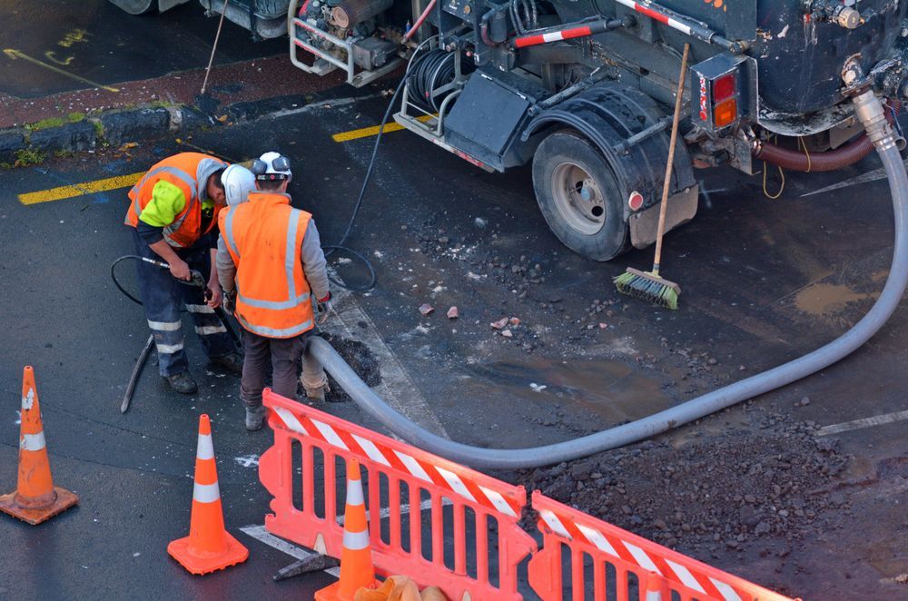 A Group Of Construction Workers Are Working On A Road Next To A Truck — All Hours Vac Truck In Mt Morgan, QLD