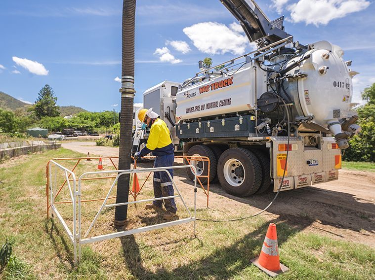 A Man Is Working On A Pipe Next To A Vacuum Truck — All Hours Vac Truck In Lakes Creek, QLD