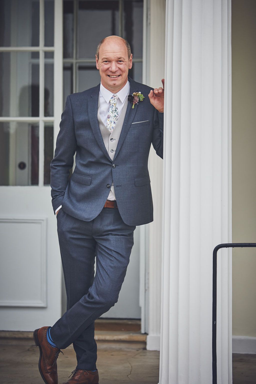 a man in a suit is leaning against a white column .