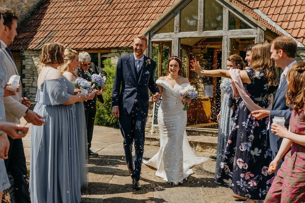 A bride and groom are walking through a crowd of people throwing confetti at them.