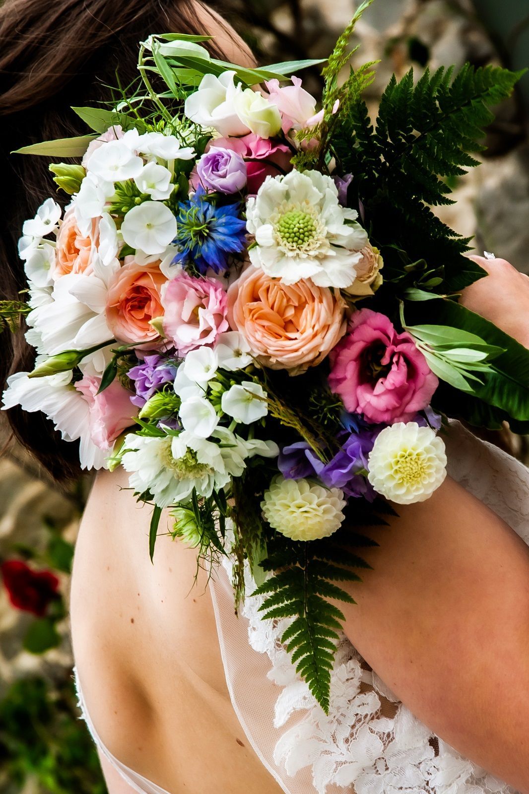 A woman in a wedding dress is holding a bouquet of flowers on her shoulder.
