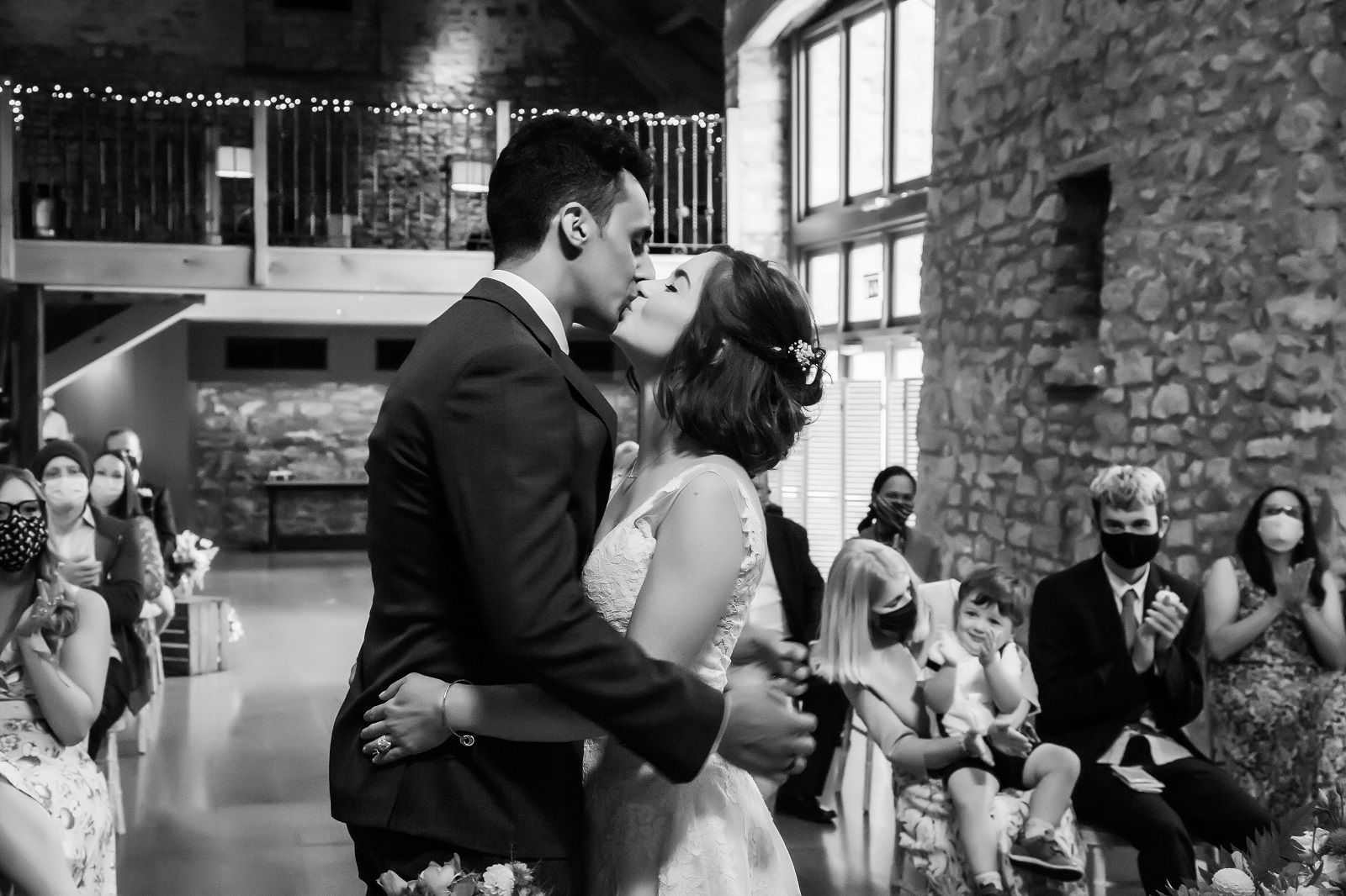 A black and white photo of a bride and groom kissing at their wedding ceremony.