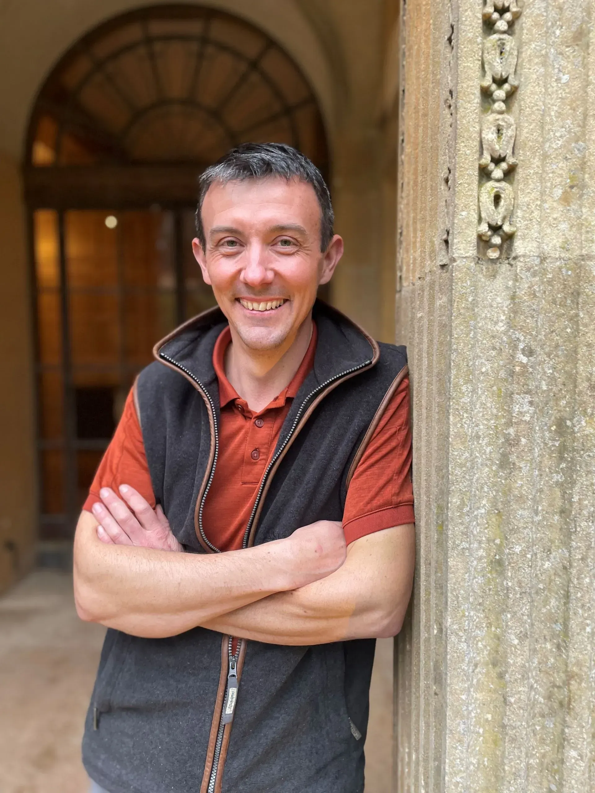 A man is leaning against a wall with his arms crossed and smiling.