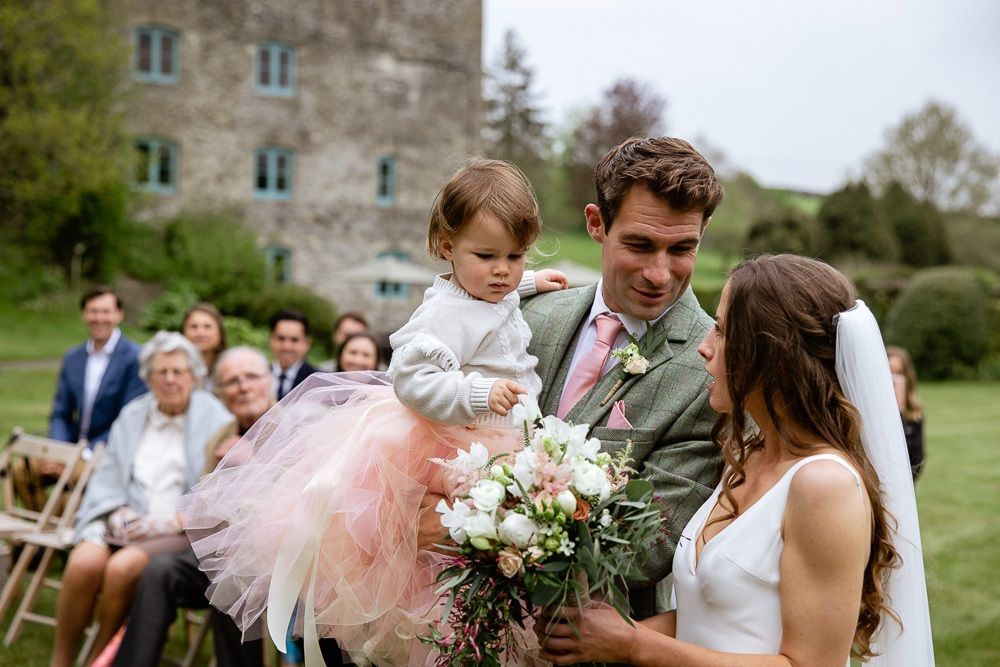 A bride and groom are holding a little girl during their wedding ceremony.