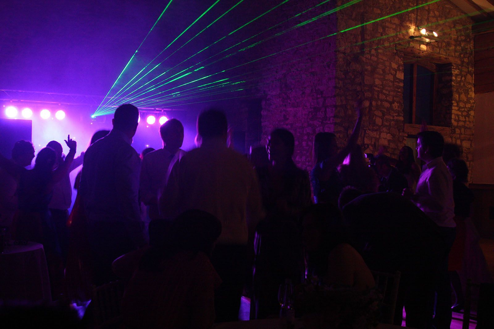 A group of people are dancing in a dark room with purple and green lights.