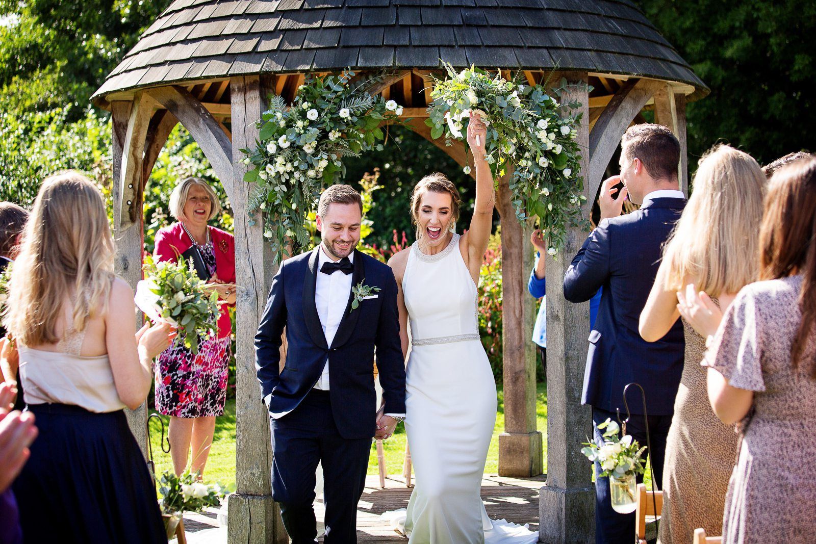 A bride and groom are walking down the aisle at their wedding under a gazebo.