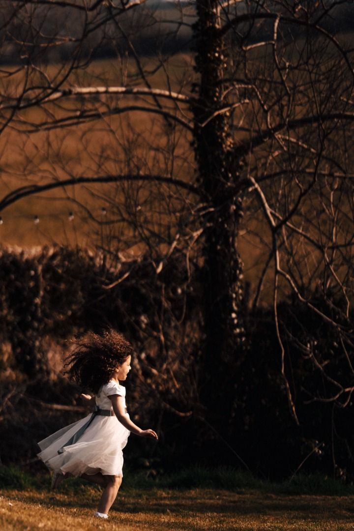 A little girl in a white dress is running in a field.