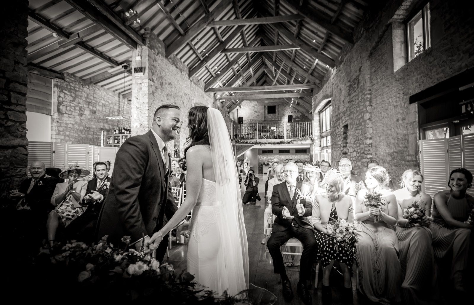 A black and white photo of a bride and groom holding hands during their wedding ceremony.