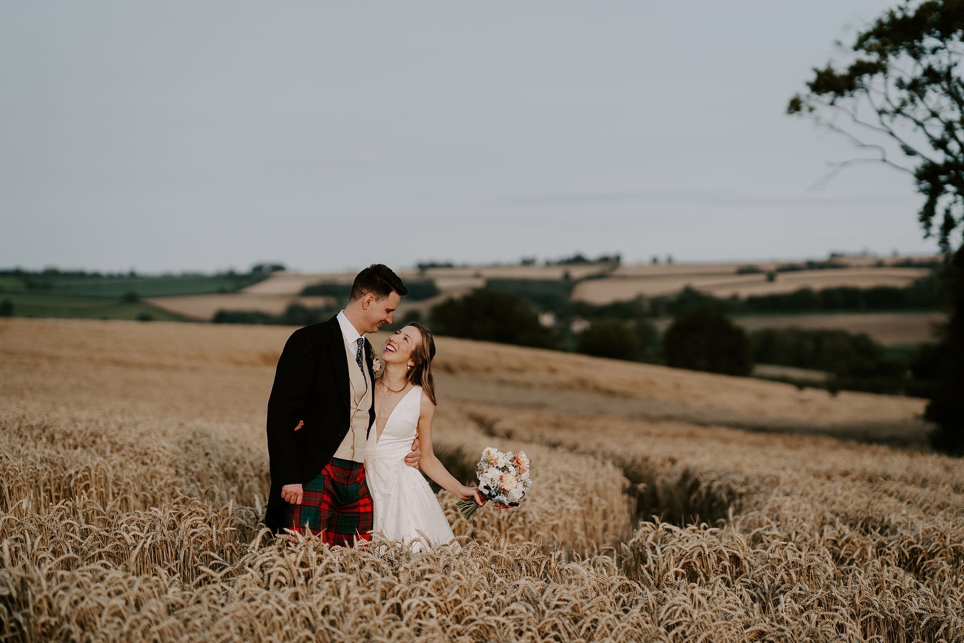 A bride and groom are standing in a field of wheat.