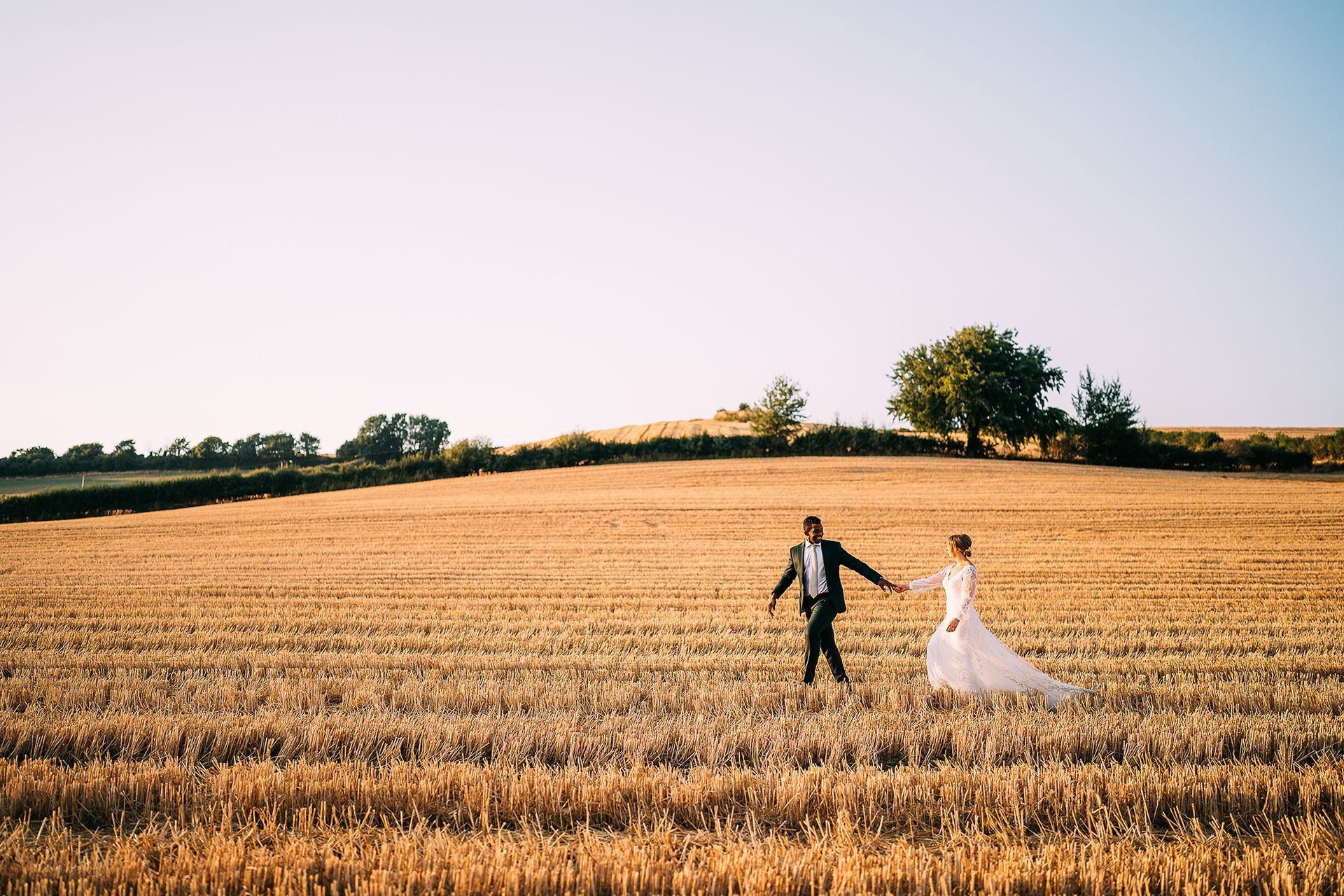 A bride and groom are walking through a field of wheat.