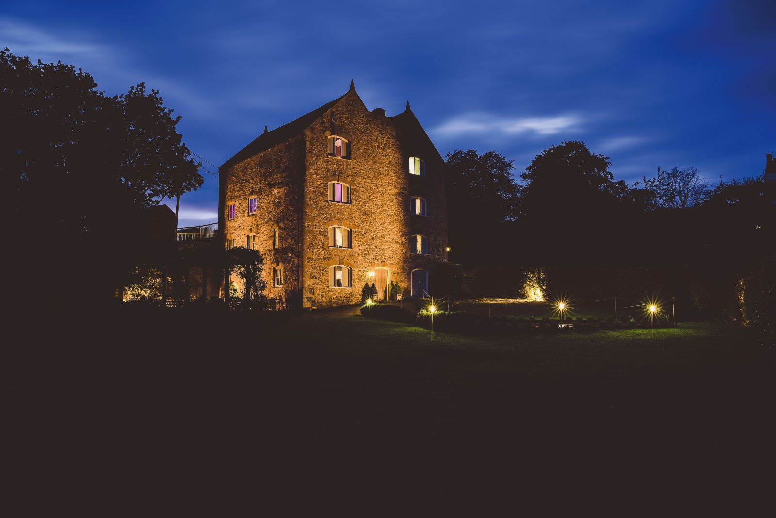 A large stone building is lit up at night surrounded by trees.