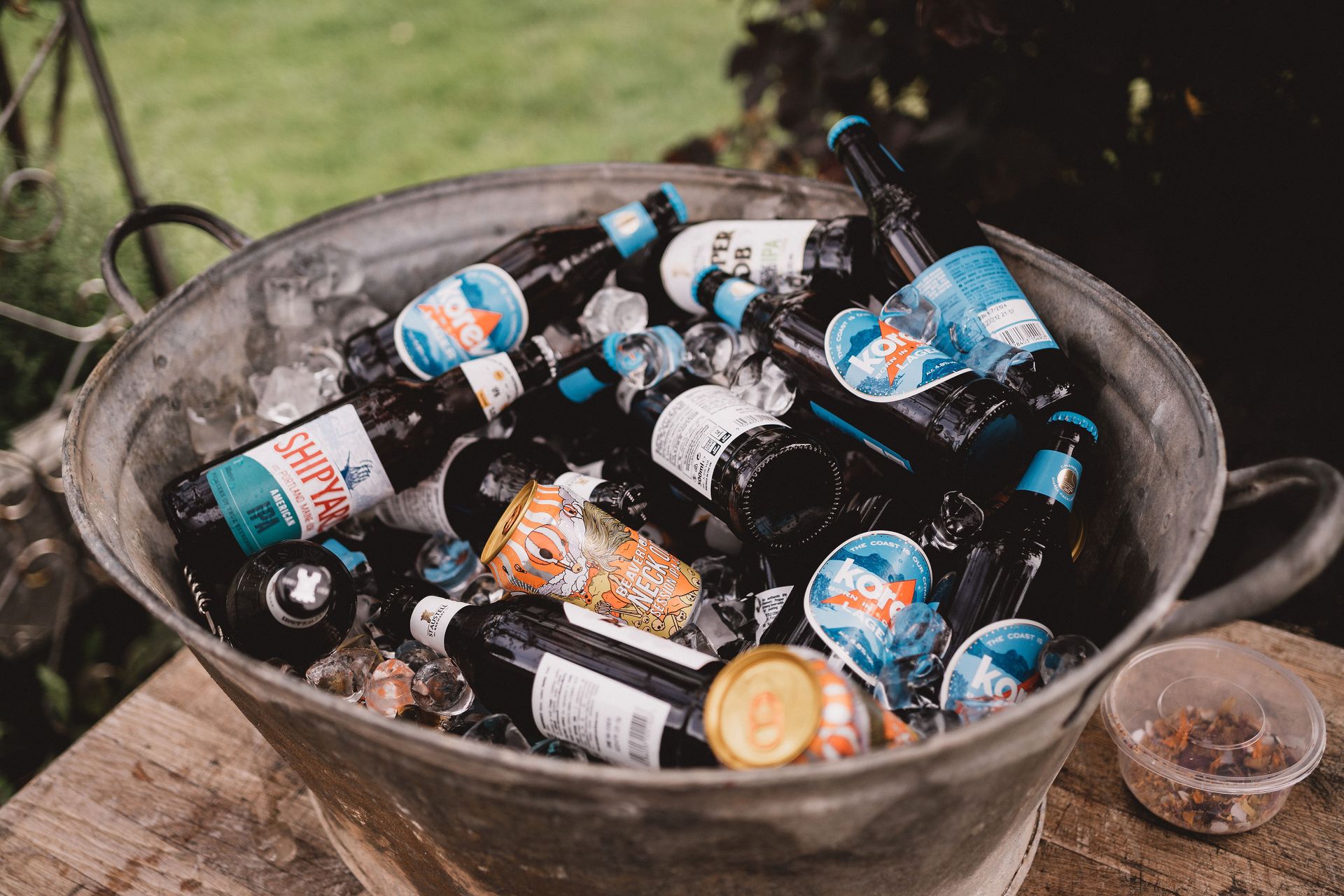A metal bucket filled with bottles of beer and ice is sitting on a wooden table.