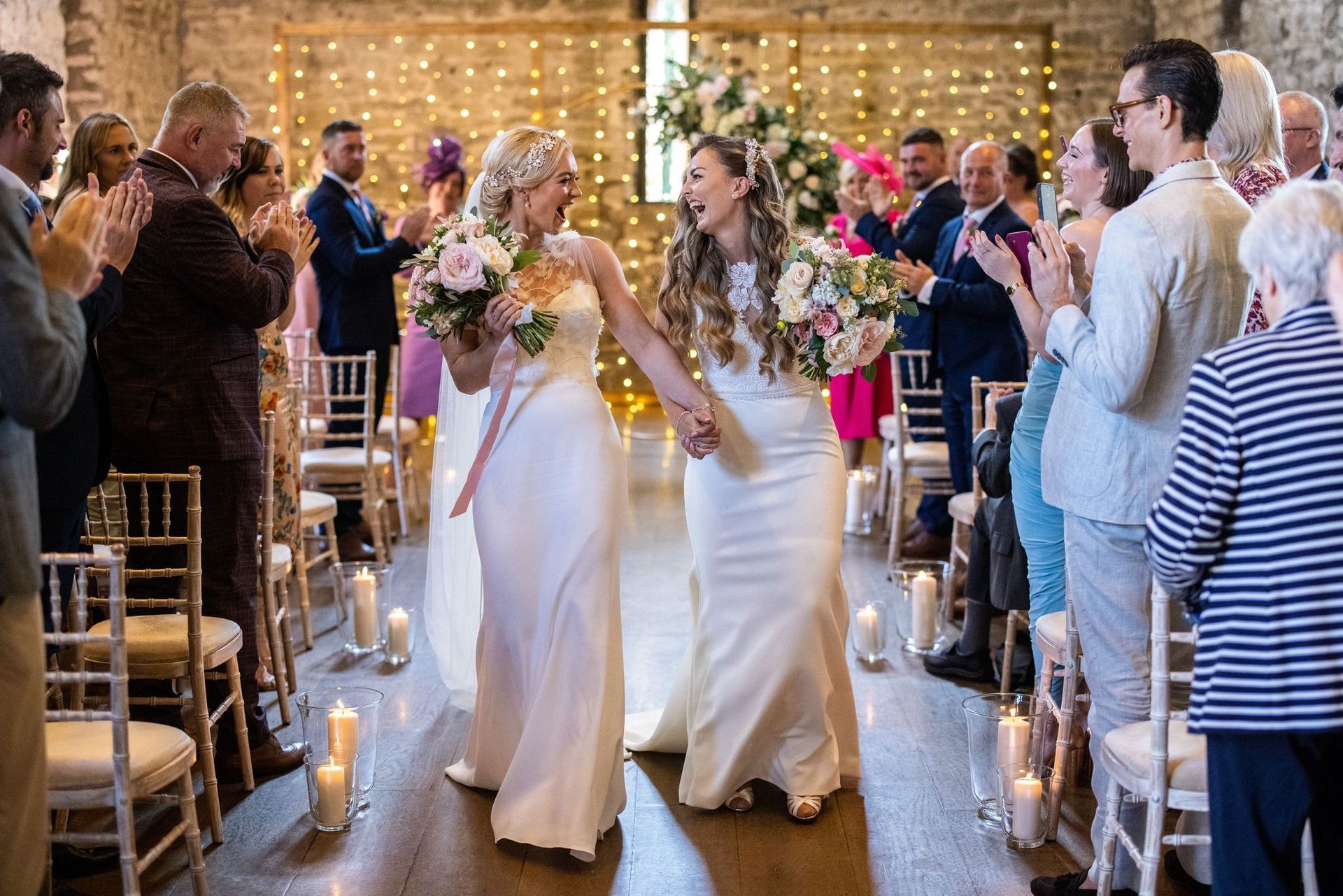 Two brides are walking down the aisle at their wedding holding hands.