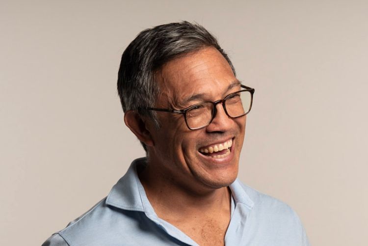 A man wearing glasses and a blue shirt is smiling.