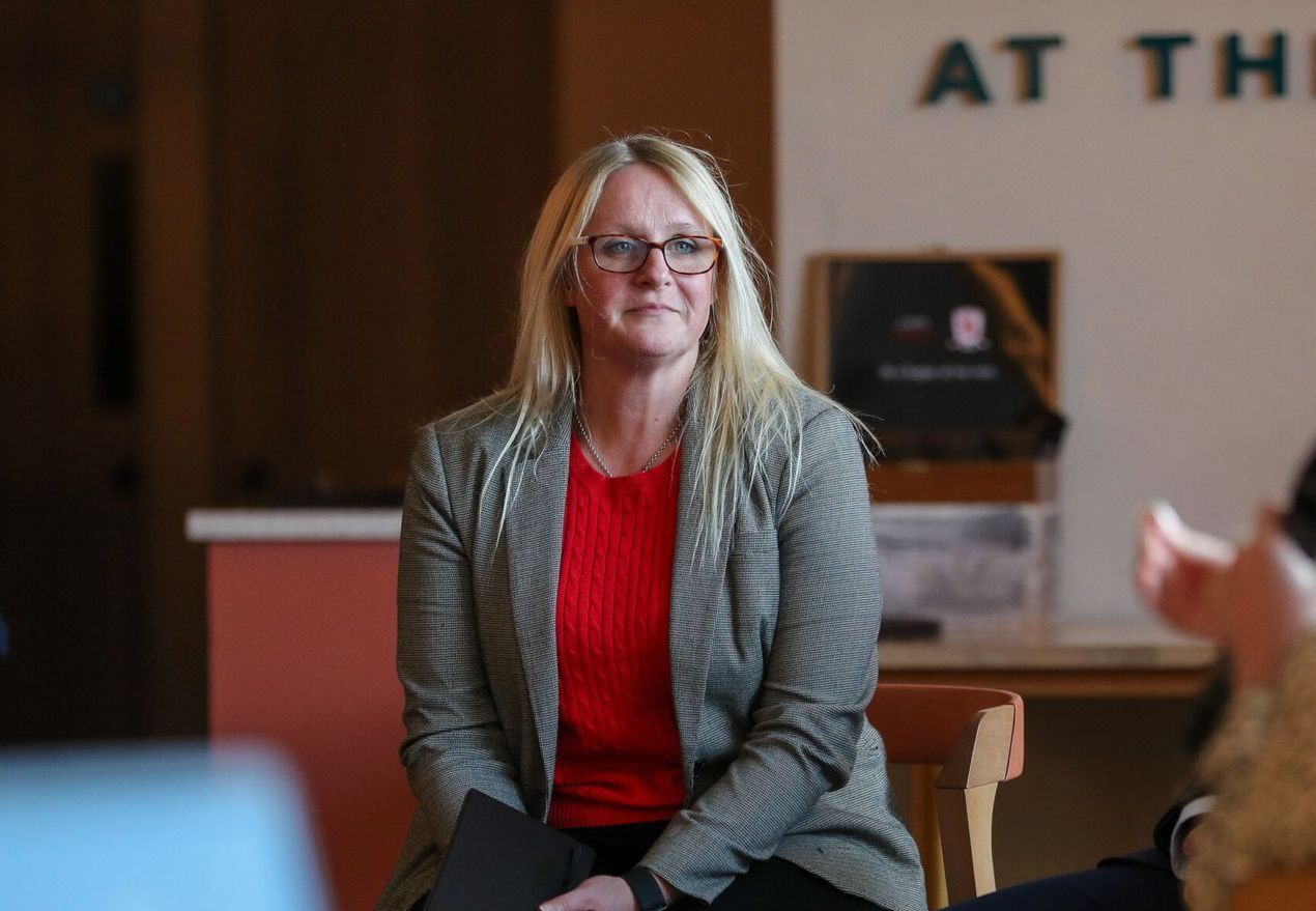 A woman wearing glasses and a red sweater is sitting on a chair.