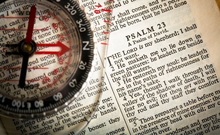 A compass lies on a Bible open to Psalm 23