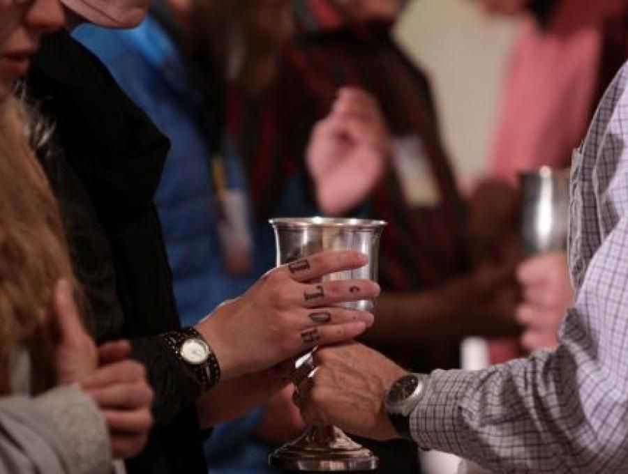 A man offers another man a silver chalice of wine
