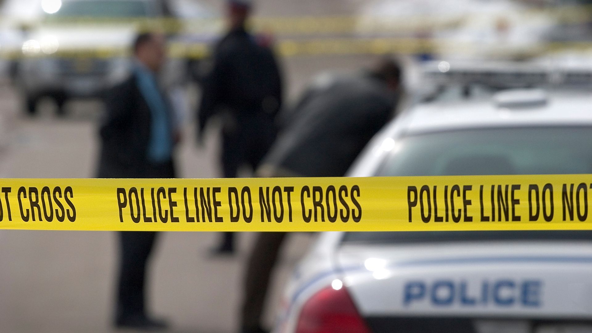 Police officers and police cars behind a yellow tape reading 