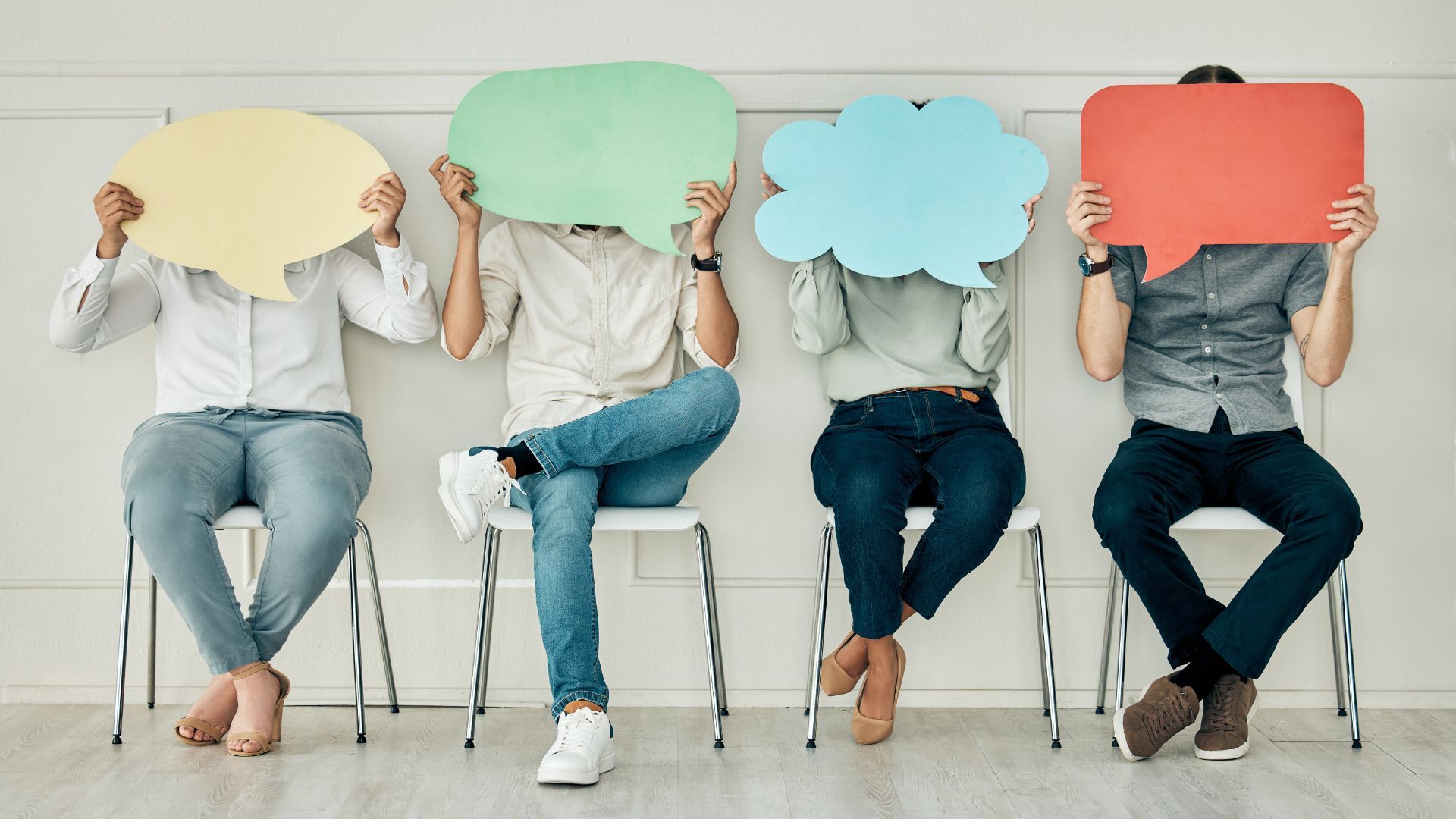 Four people sit in chairs covering their faces with speech bubbles