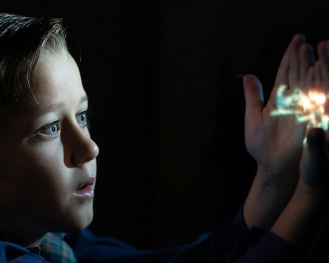 young boy with hands close to his face watching a film on his hands