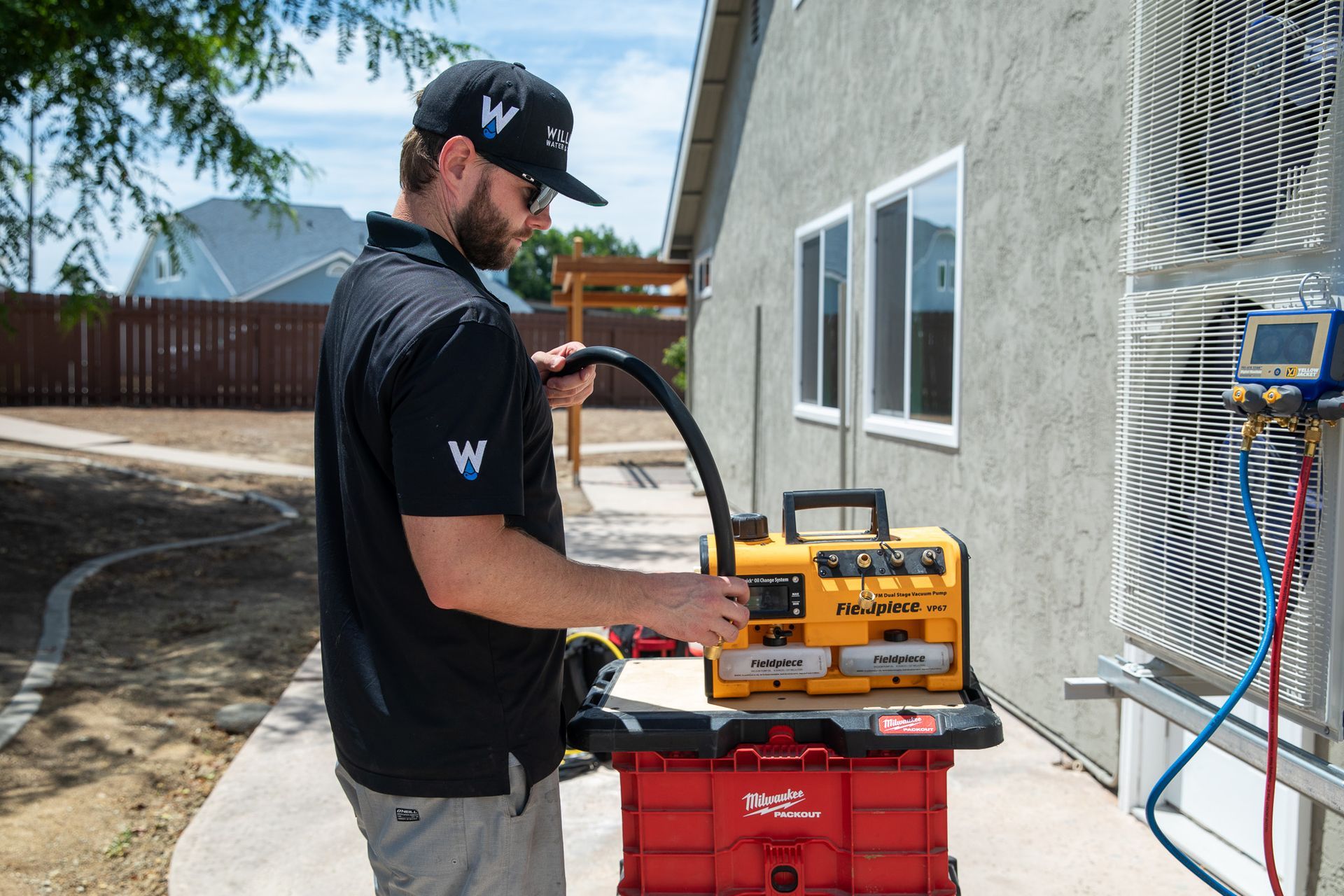 HVAC technician working on AC unit outdoors. Yellow and black equipment, red tool case.