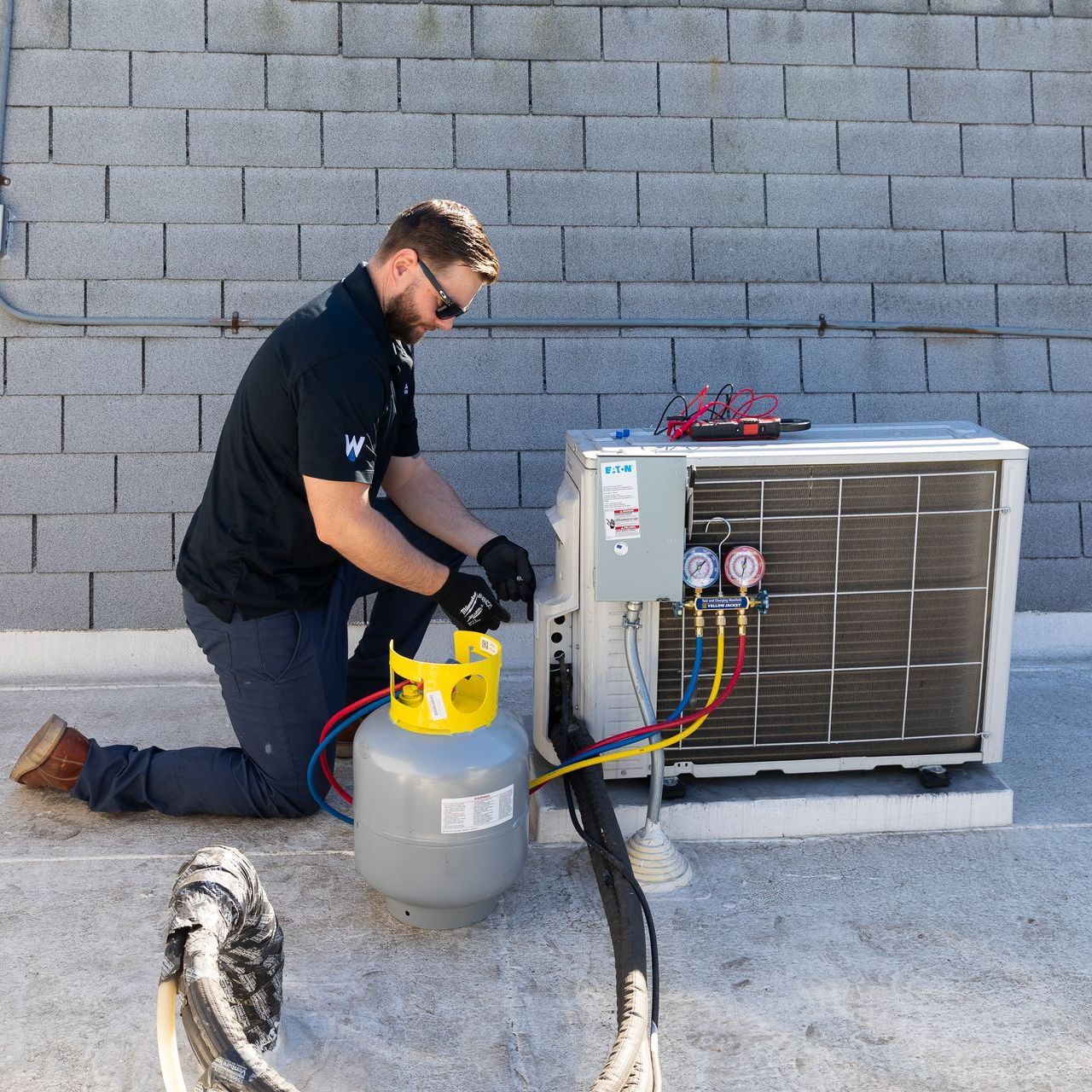 A man is kneeling down next to a propane tank