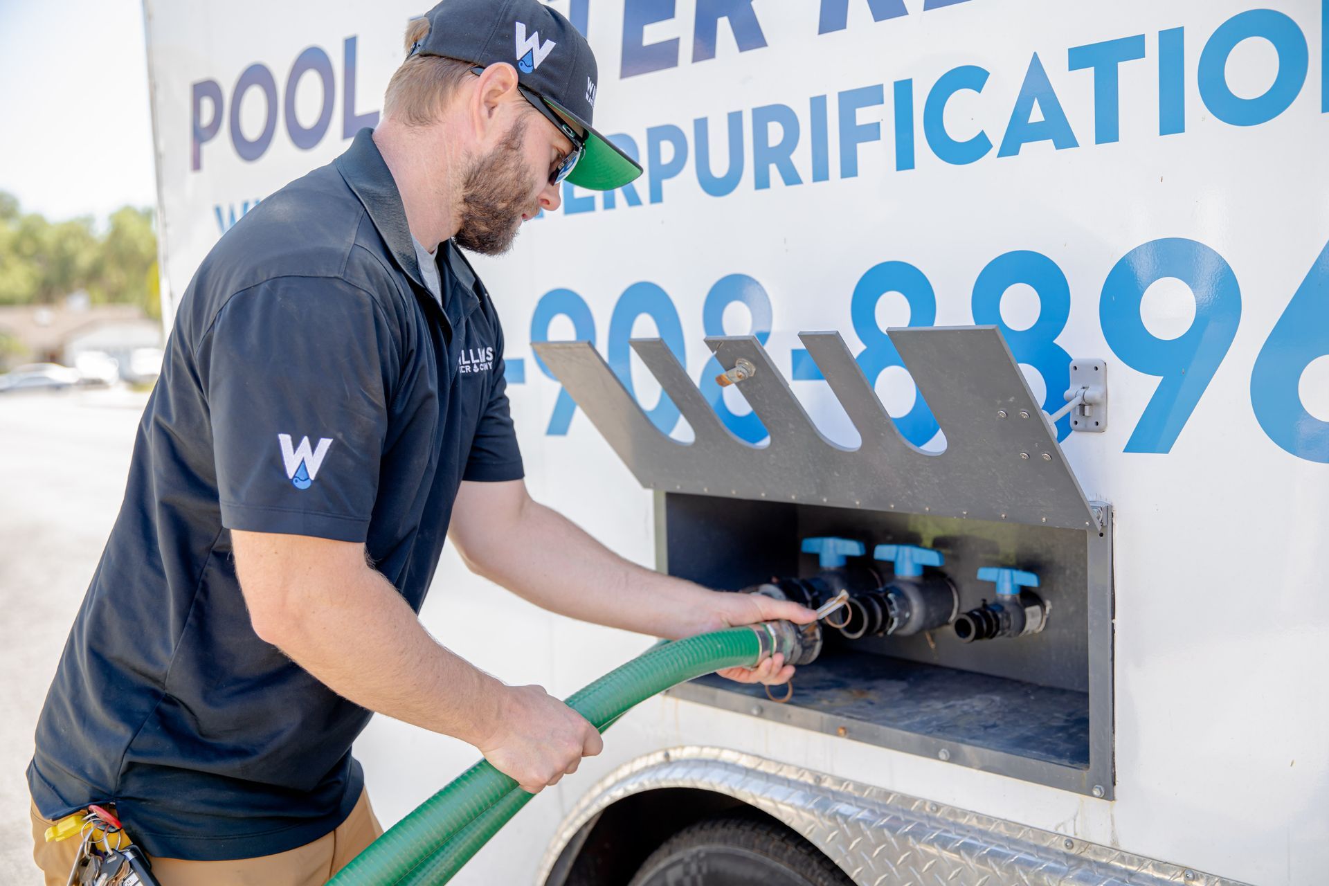 Man in navy shirt connects a green hose to a truck labeled