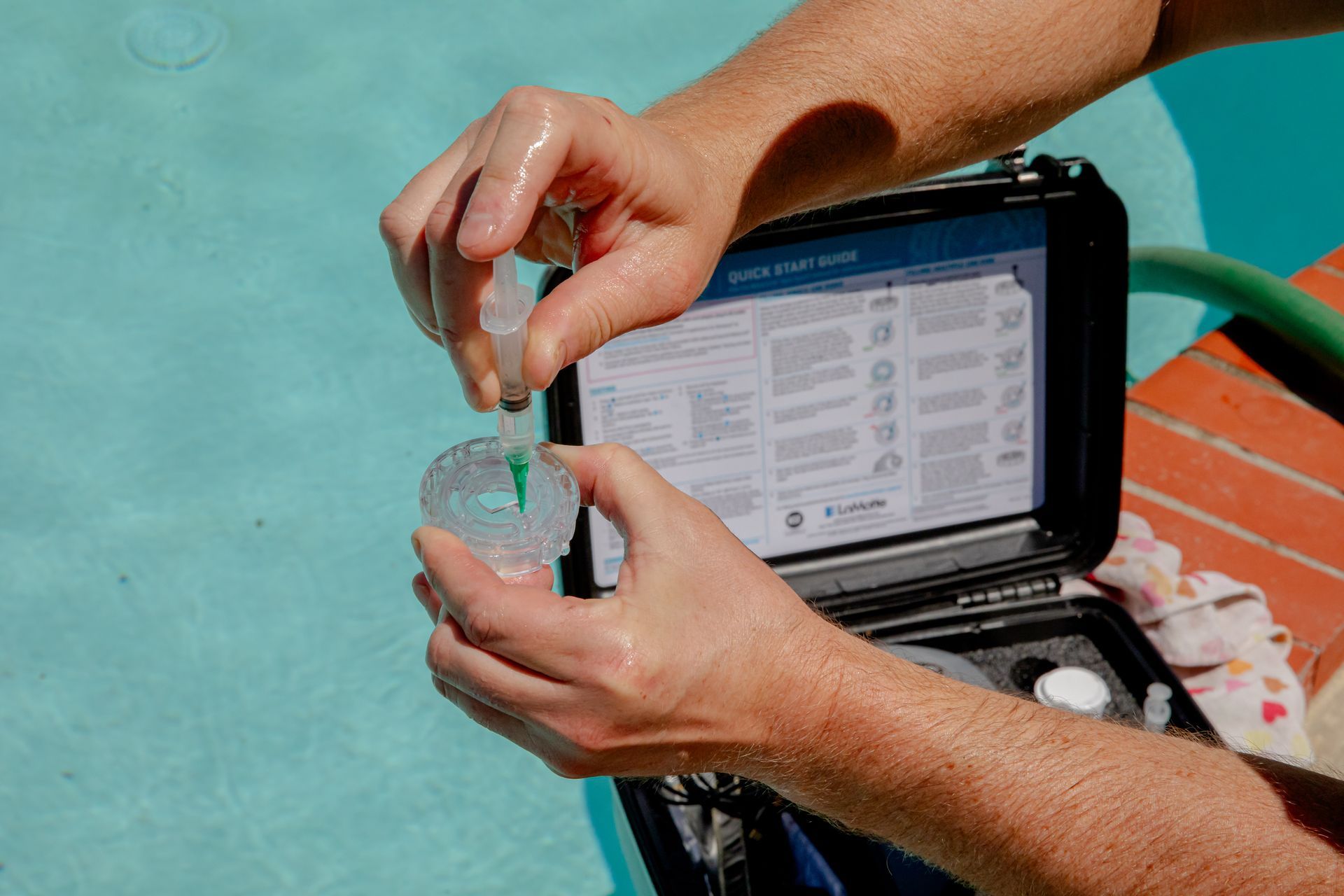 Person testing pool water with dropper and kit near the pool.