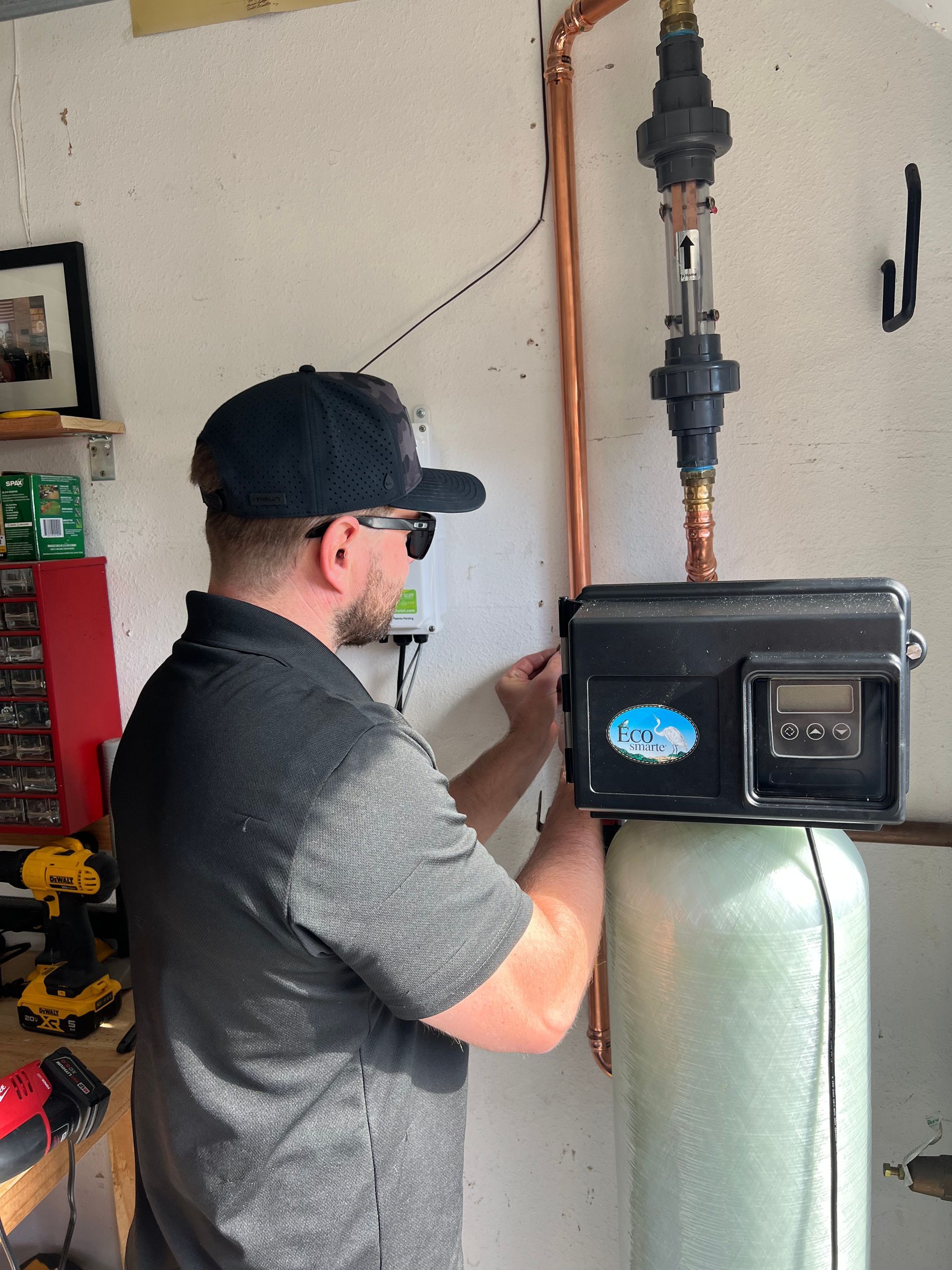 Man smiles while using a red tool on copper pipes near a white panel. Inside a workshop.