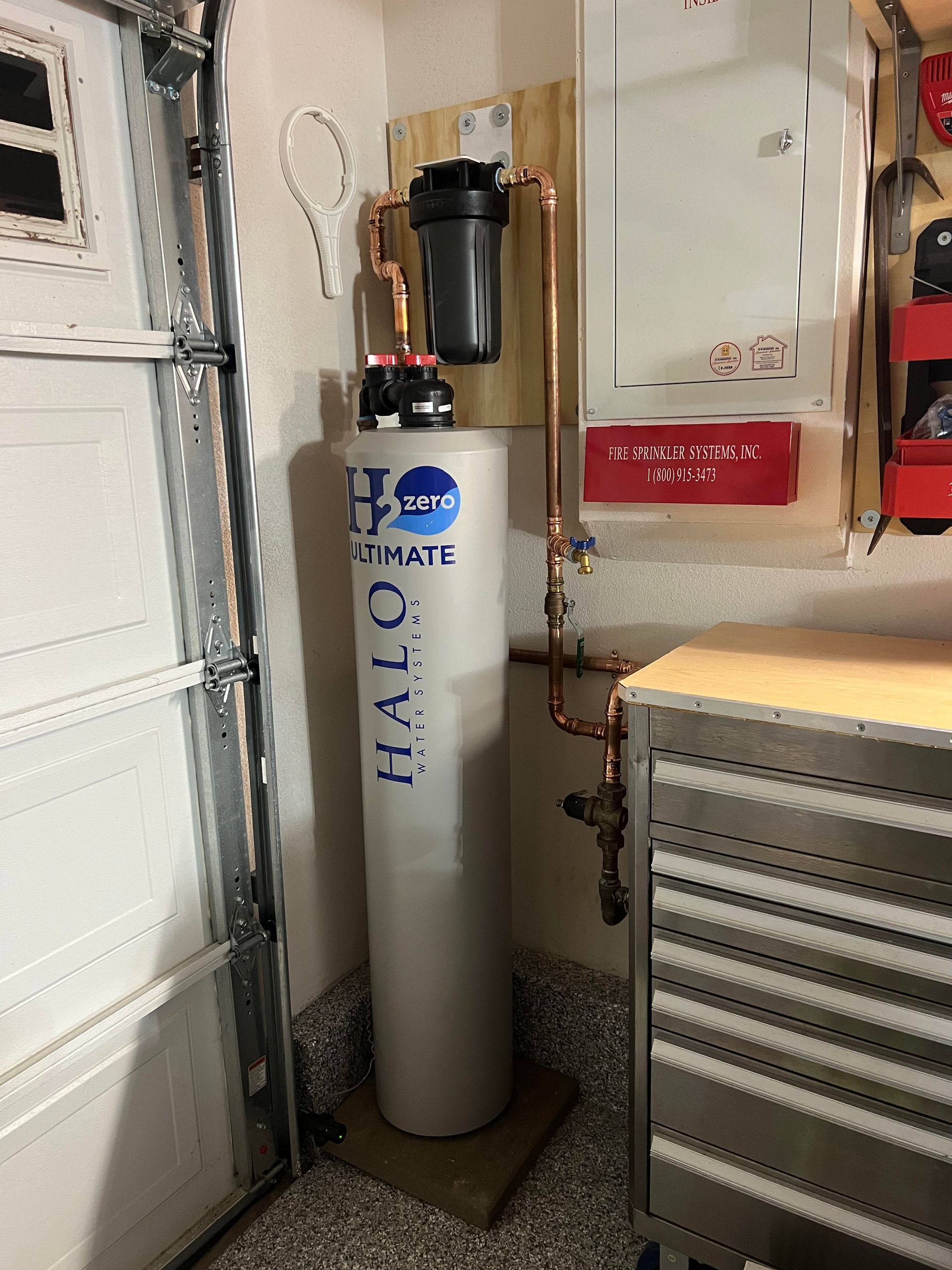 Water filtration system installed in a garage. The system is white, black and copper colored.