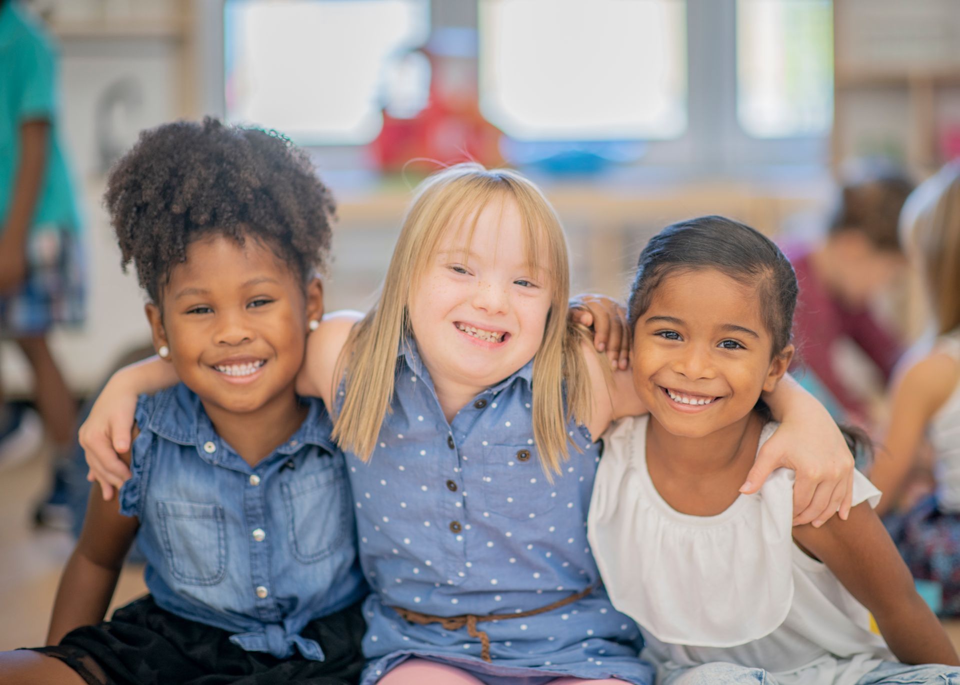 Three smiling girls and sitting together with arms wrapped around one another