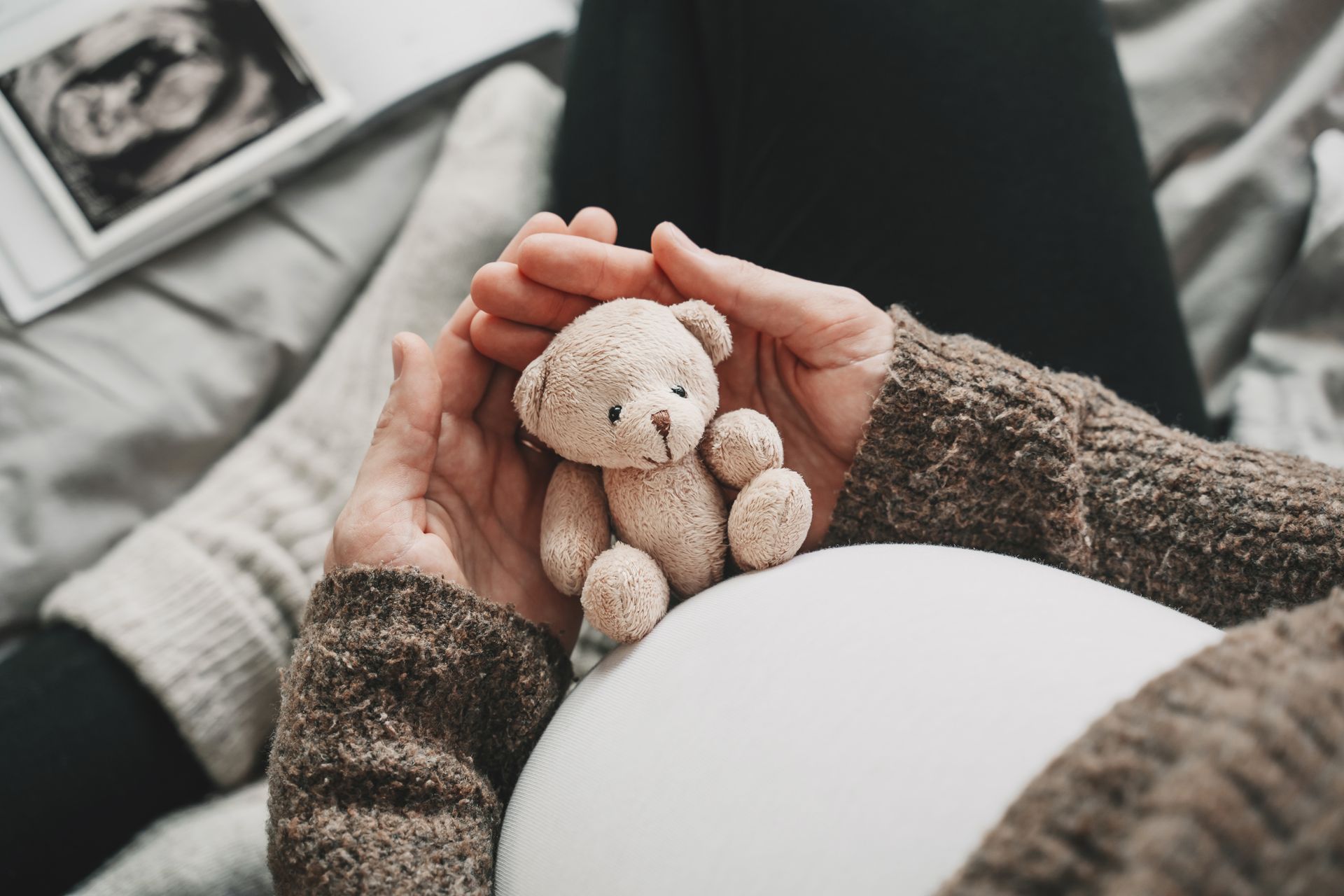 A pregnant woman is looking at a teddy bear