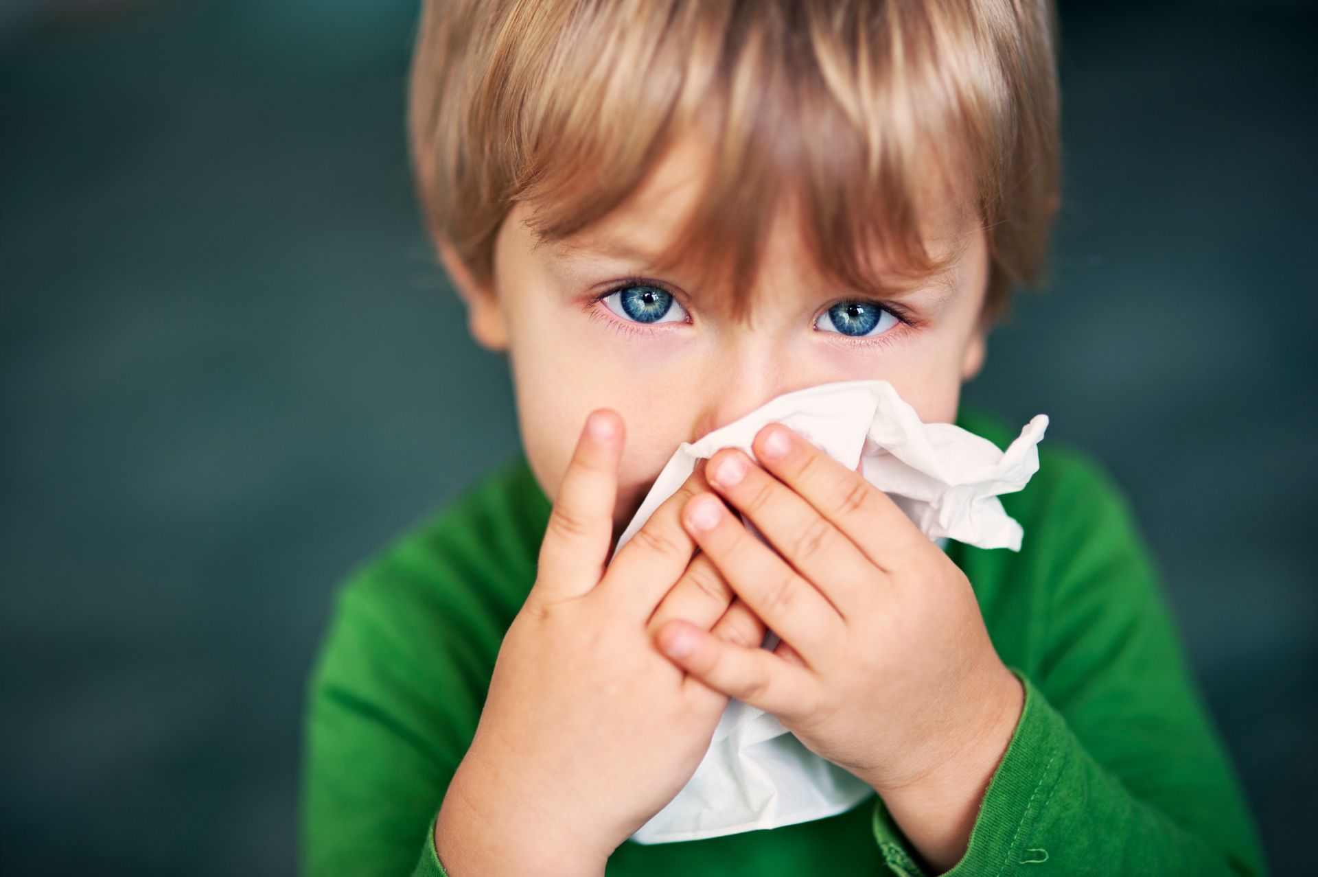 A boy is blowing his nose with a tissue