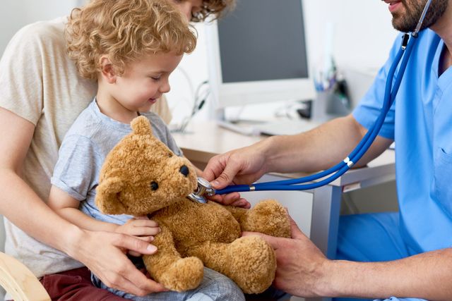 Doctor examining a child with a teddy bear in a clinic waiting room