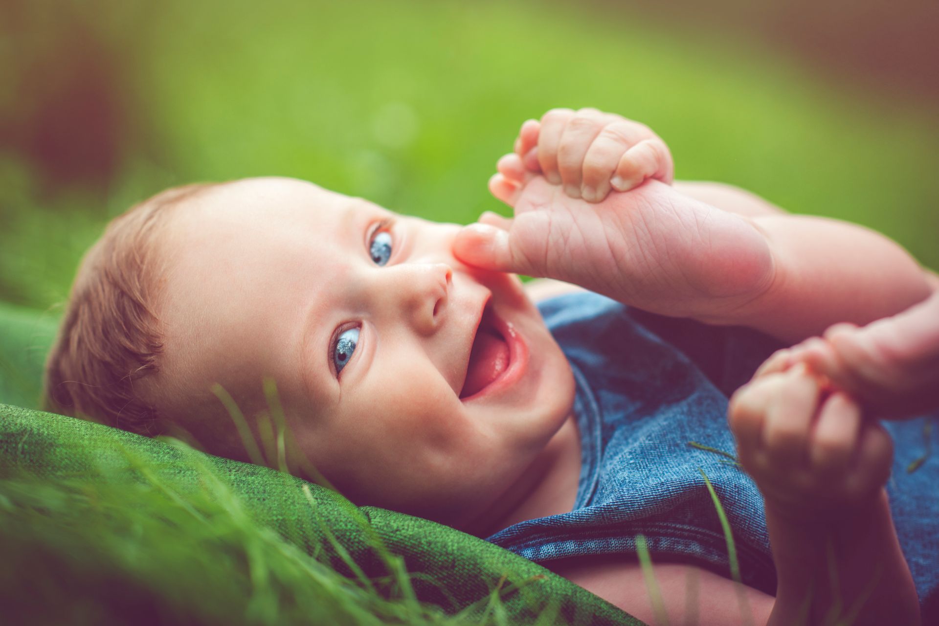 A smiling, laughing baby is lying in the grass