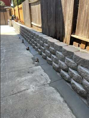 A stone wall is being built next to a wooden fence.