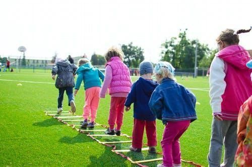 A group of children are walking across a ladder on a field.