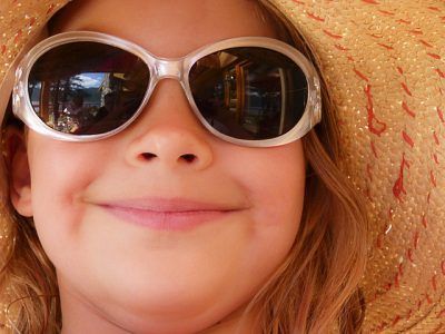 A little girl wearing sunglasses and a hat is smiling.