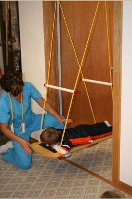 A woman is kneeling next to a child laying on a swing.