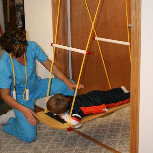 A woman is kneeling next to a child laying on a swing